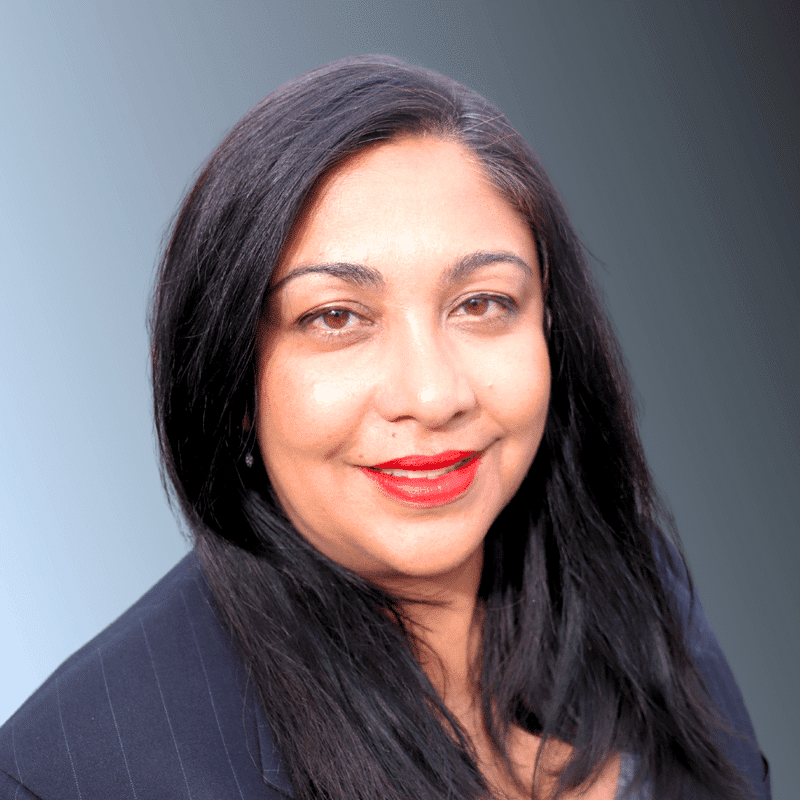 photo of smiling woman with shaded background. She has long dark hair, bright red lipstick, and is smiling.